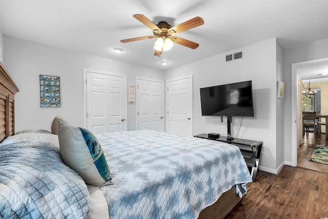 bedroom featuring ceiling fan with notable chandelier, two closets, and dark wood-type flooring