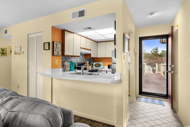 kitchen featuring kitchen peninsula, stainless steel fridge, sink, light tile patterned floors, and cream cabinetry