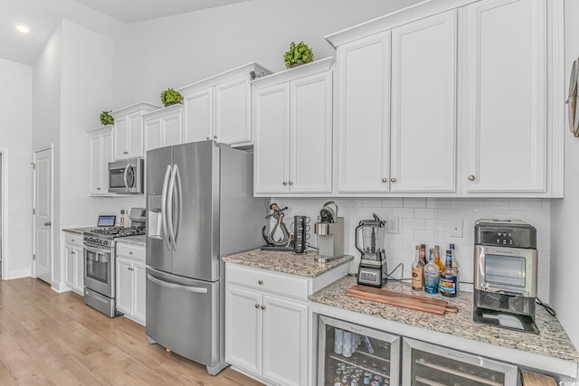 kitchen with light wood finished floors, decorative backsplash, appliances with stainless steel finishes, white cabinetry, and beverage cooler