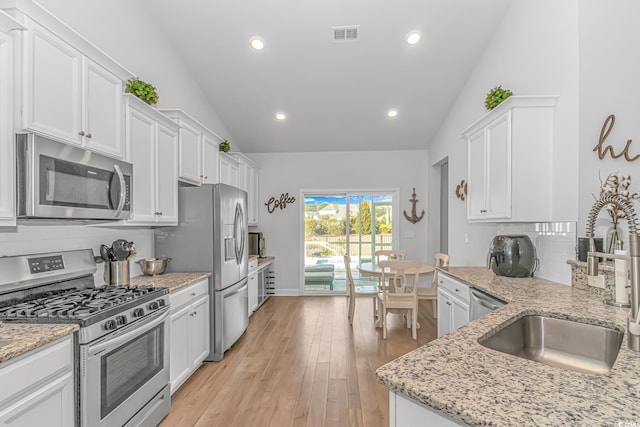 kitchen with lofted ceiling, light wood-style flooring, a sink, white cabinets, and appliances with stainless steel finishes