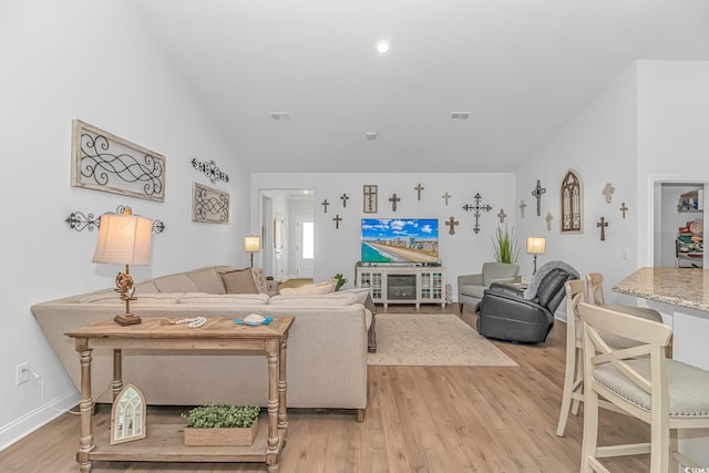 living area with lofted ceiling, baseboards, visible vents, and light wood finished floors