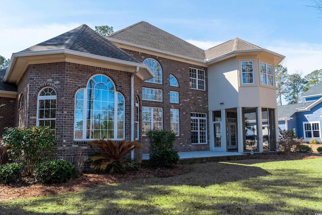 view of front of house featuring a front yard, a patio area, brick siding, and roof with shingles