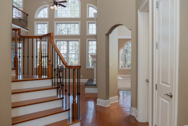 stairs with arched walkways, a high ceiling, wood finished floors, and a healthy amount of sunlight