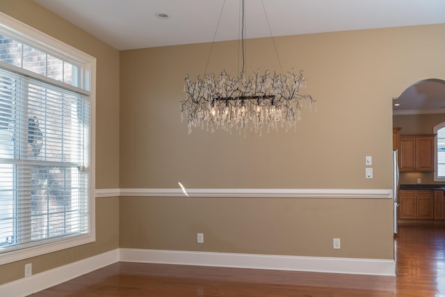 unfurnished dining area with arched walkways, dark wood-style flooring, a healthy amount of sunlight, and baseboards