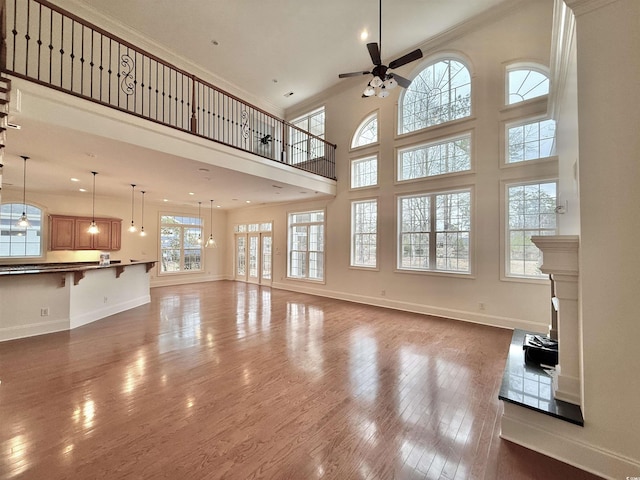 unfurnished living room featuring baseboards, ornamental molding, hardwood / wood-style floors, a high ceiling, and a ceiling fan