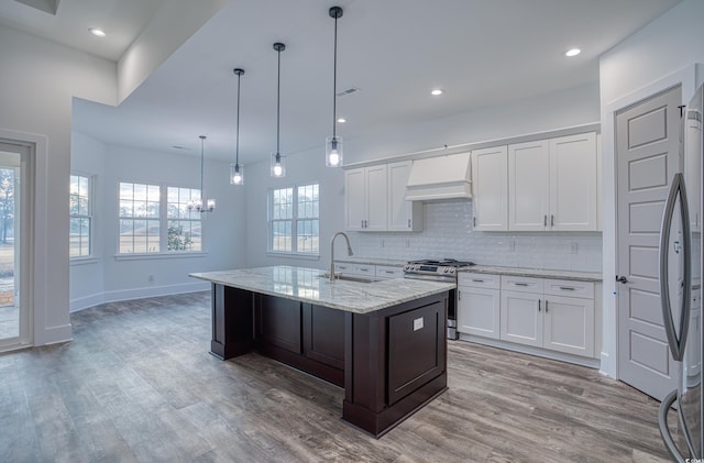 kitchen featuring custom exhaust hood, sink, a kitchen island with sink, appliances with stainless steel finishes, and white cabinets