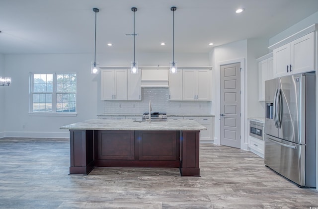 kitchen featuring decorative light fixtures, white cabinetry, a kitchen island with sink, light wood-type flooring, and stainless steel appliances