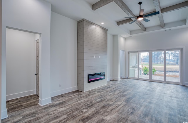 unfurnished living room featuring wood-type flooring, beamed ceiling, a large fireplace, ceiling fan, and coffered ceiling