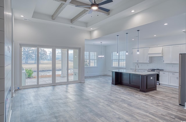 kitchen with a center island with sink, custom exhaust hood, decorative backsplash, white cabinetry, and appliances with stainless steel finishes