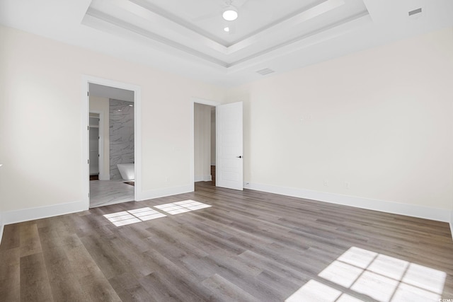 unfurnished bedroom with ensuite bath, baseboards, a raised ceiling, and wood finished floors