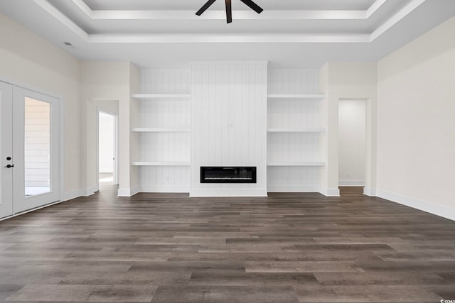 unfurnished living room with a fireplace, a tray ceiling, dark wood-type flooring, and french doors