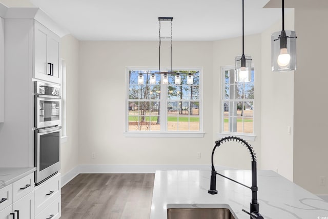 kitchen with white cabinets, wood finished floors, hanging light fixtures, light stone countertops, and stainless steel double oven