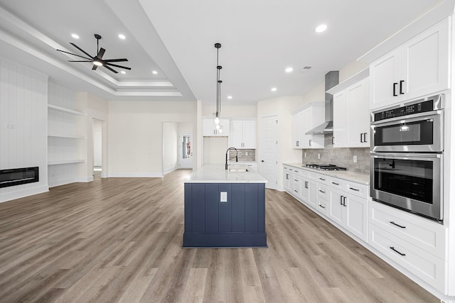 kitchen with decorative light fixtures, open floor plan, white cabinetry, an island with sink, and wall chimney exhaust hood