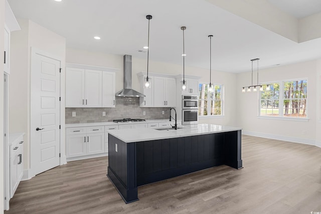 kitchen with wall chimney exhaust hood, a center island with sink, white cabinets, and light countertops