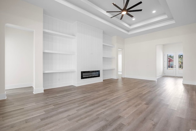 unfurnished living room featuring built in features, heating unit, a raised ceiling, light wood-style flooring, and a large fireplace