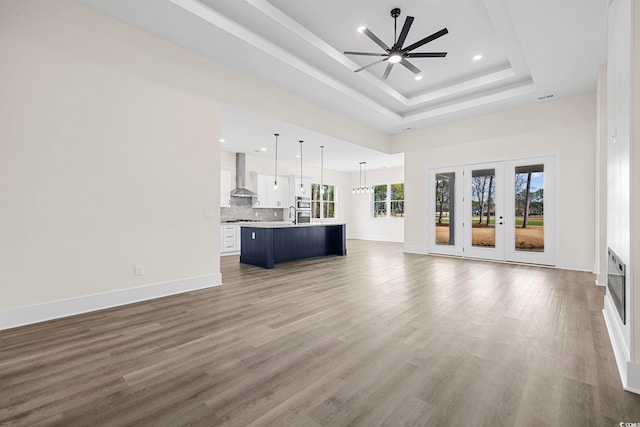 unfurnished living room with a tray ceiling, recessed lighting, a ceiling fan, wood finished floors, and baseboards