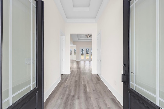 corridor with baseboards, a raised ceiling, ornamental molding, french doors, and light wood-type flooring