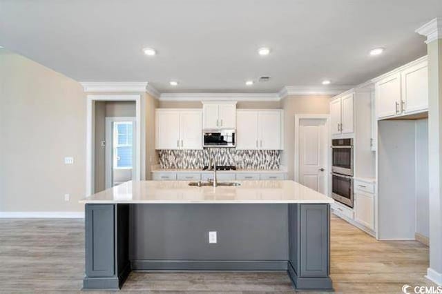 kitchen featuring tasteful backsplash, white cabinets, an island with sink, and stainless steel appliances