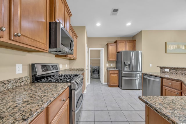 kitchen with stone countertops, light tile patterned floors, stainless steel appliances, and washing machine and clothes dryer