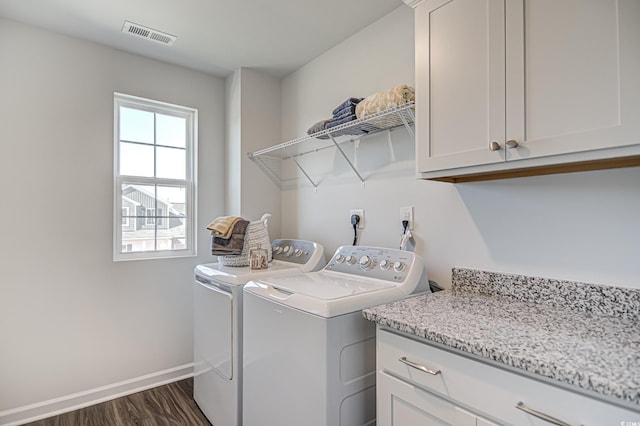 clothes washing area with washer and clothes dryer, visible vents, cabinet space, dark wood-type flooring, and baseboards