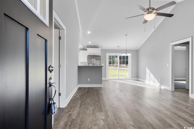 unfurnished living room with wood-type flooring, crown molding, ceiling fan with notable chandelier, and high vaulted ceiling