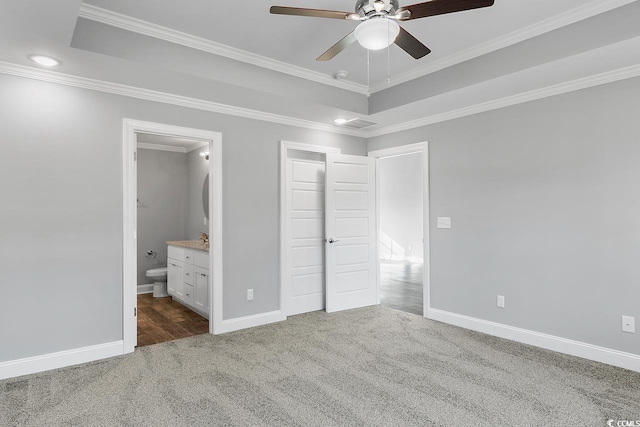 unfurnished bedroom with ceiling fan, ensuite bathroom, a tray ceiling, carpet floors, and ornamental molding