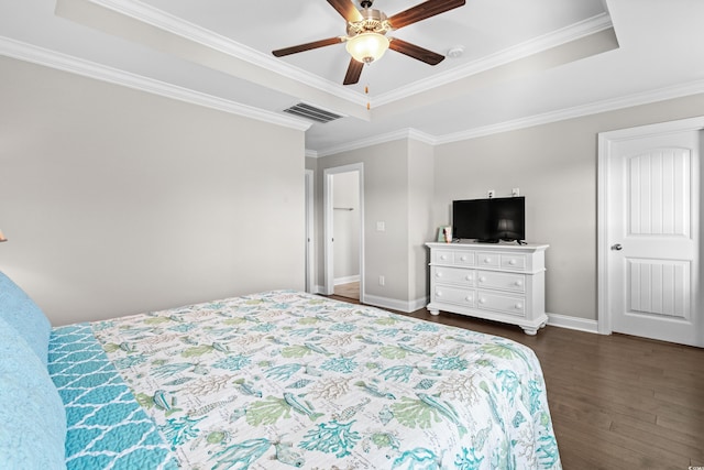 bedroom with dark wood-type flooring, ceiling fan, ornamental molding, and a tray ceiling