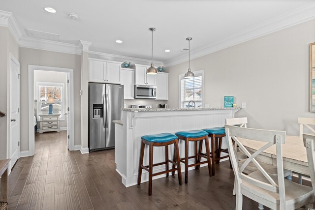 kitchen with light stone countertops, white cabinets, stainless steel appliances, ornamental molding, and a breakfast bar area