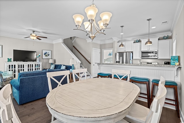 dining area featuring dark wood-type flooring, ornamental molding, and ceiling fan with notable chandelier