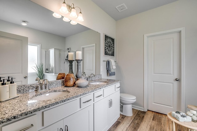 bathroom with toilet, an inviting chandelier, wood-type flooring, vanity, and a shower with door