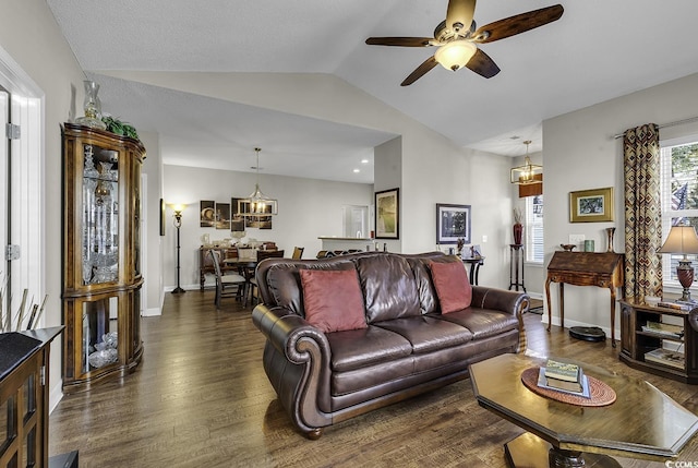 living room with ceiling fan with notable chandelier, vaulted ceiling, and dark wood-type flooring