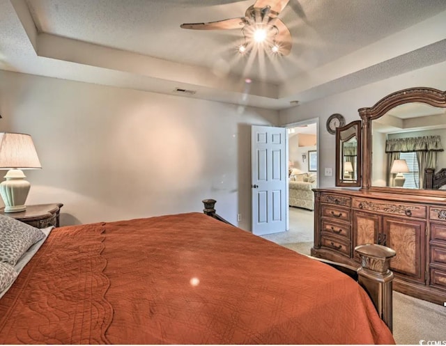 bedroom featuring ceiling fan, light colored carpet, a raised ceiling, and a textured ceiling