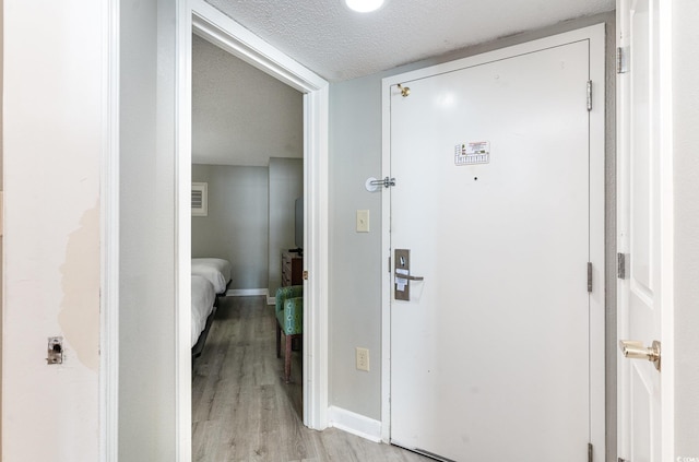 corridor with a textured ceiling and light wood-type flooring