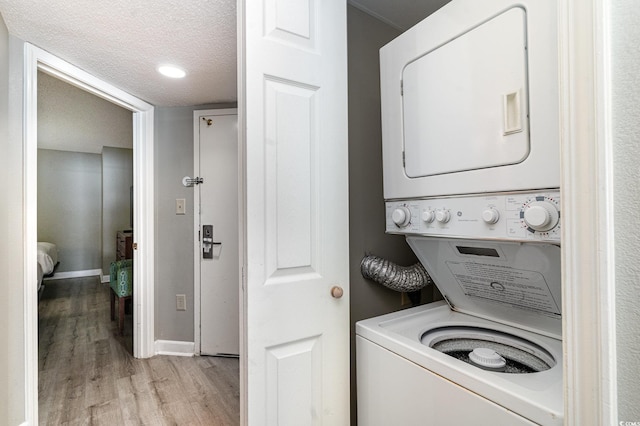 laundry room with stacked washer / dryer, light hardwood / wood-style floors, and a textured ceiling