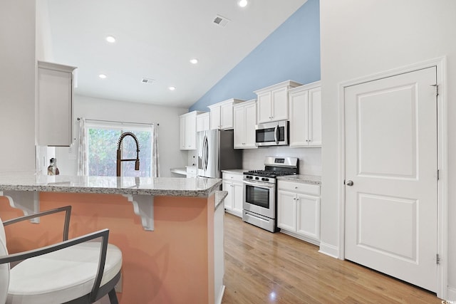 kitchen with light stone counters, a kitchen breakfast bar, white cabinetry, and appliances with stainless steel finishes