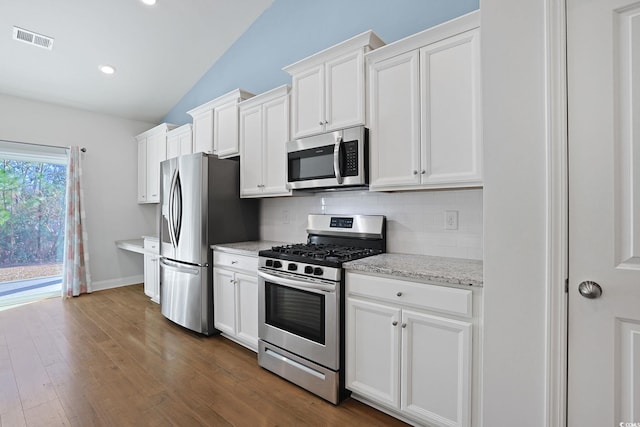 kitchen with lofted ceiling, backsplash, white cabinetry, stainless steel appliances, and light stone counters