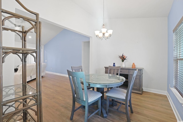 dining space featuring light wood-type flooring, a notable chandelier, and vaulted ceiling