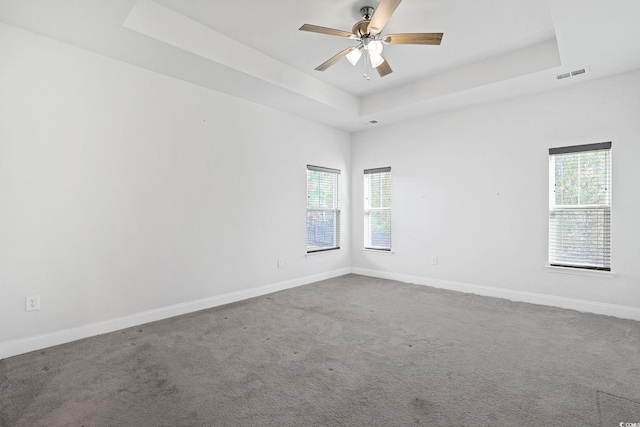 carpeted empty room with ceiling fan, a healthy amount of sunlight, and a raised ceiling