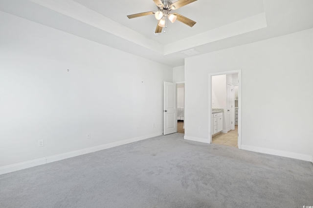 unfurnished bedroom with ceiling fan, light carpet, a tray ceiling, and connected bathroom