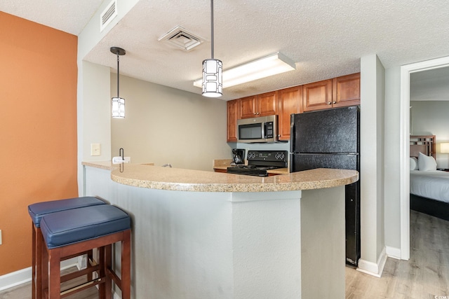 kitchen featuring kitchen peninsula, pendant lighting, light hardwood / wood-style floors, a kitchen bar, and black appliances