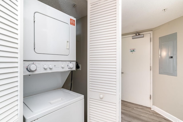 laundry room with stacked washer / drying machine, light wood-type flooring, a textured ceiling, and electric panel