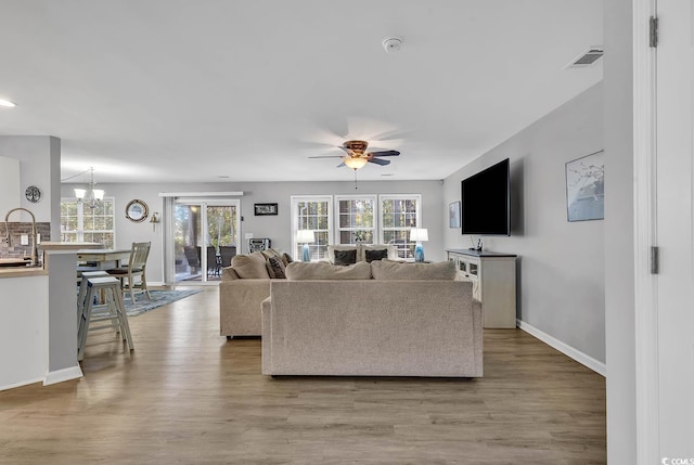 living room with ceiling fan with notable chandelier, a wealth of natural light, and light wood-type flooring