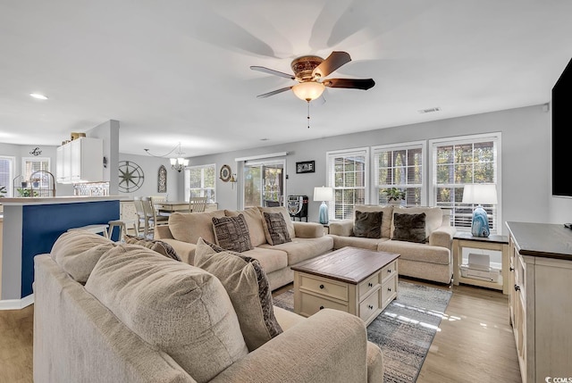 living room with ceiling fan with notable chandelier and light hardwood / wood-style floors