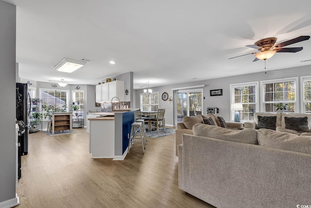 living room featuring ceiling fan with notable chandelier and light hardwood / wood-style flooring