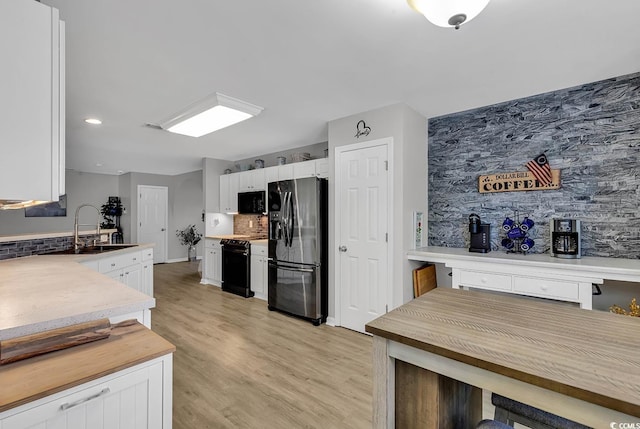 kitchen featuring sink, white cabinets, backsplash, black appliances, and light wood-type flooring