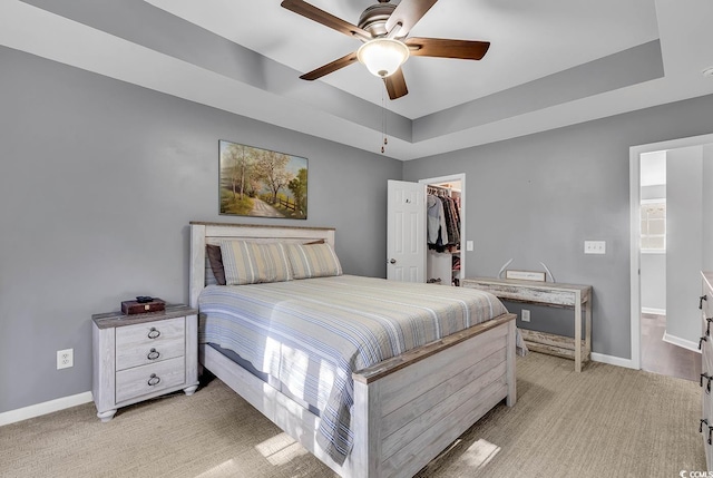 carpeted bedroom featuring ceiling fan, a walk in closet, a tray ceiling, and a closet