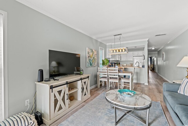 living room featuring sink, light wood-type flooring, and ornamental molding