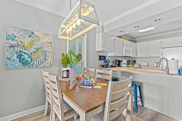 dining room with light wood-type flooring, crown molding, and sink