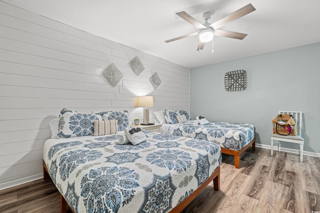 bedroom featuring wood-type flooring, ceiling fan, and wooden walls