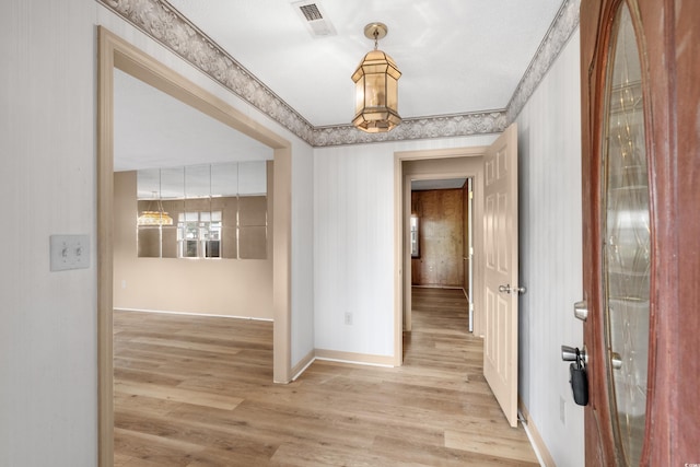 hall featuring a chandelier, light wood-type flooring, visible vents, and baseboards